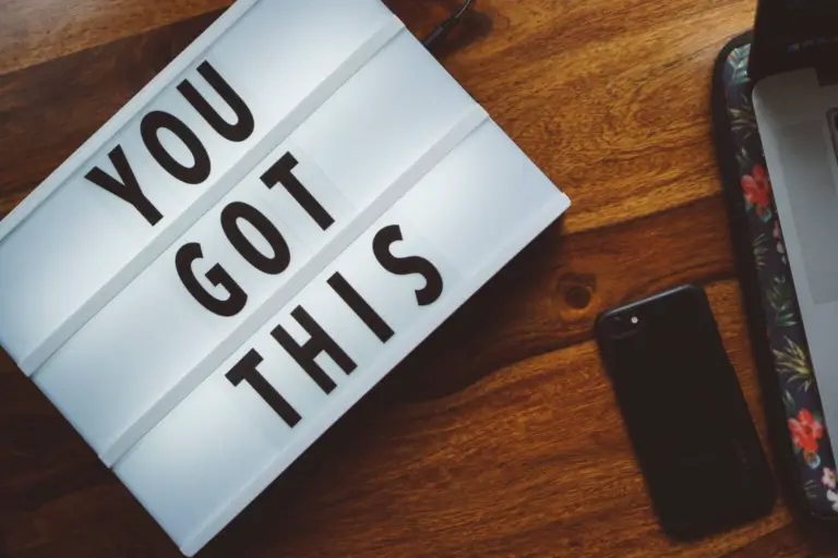 Black and white "You got this" sign on a table next to a laptop and iPhone