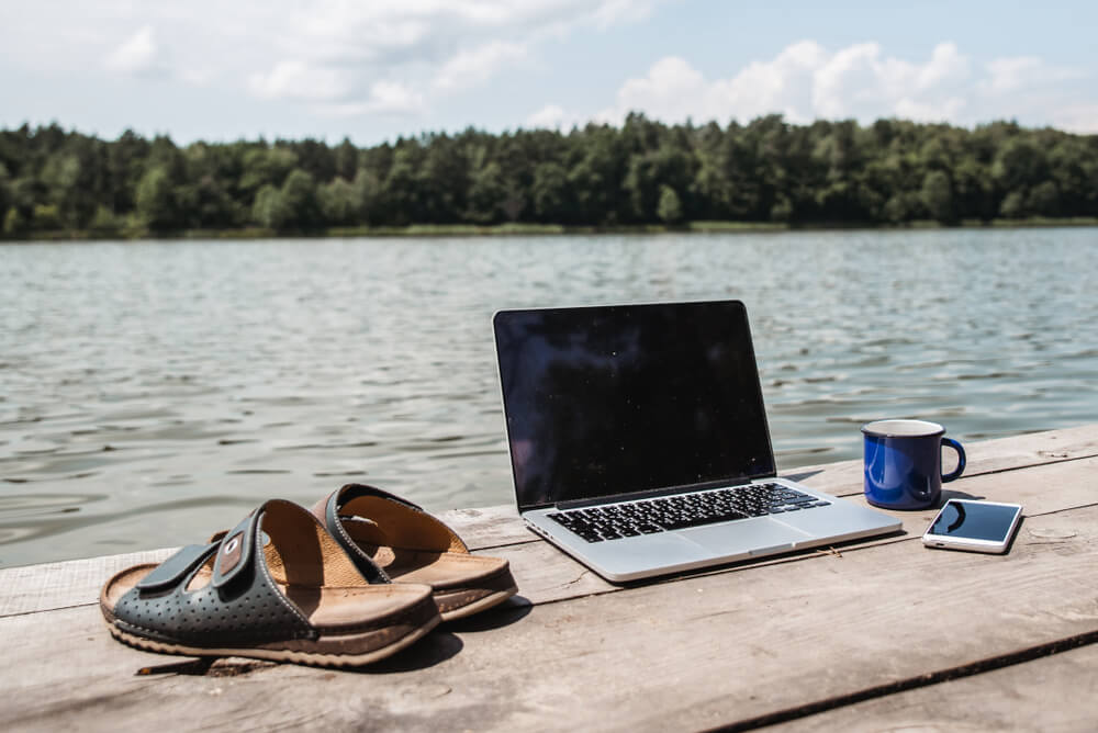 Photo of a laptop, coffee cup, and sandals on a dock facing a peaceful summer lake, Switch to TypeWell from C-Print this summer.