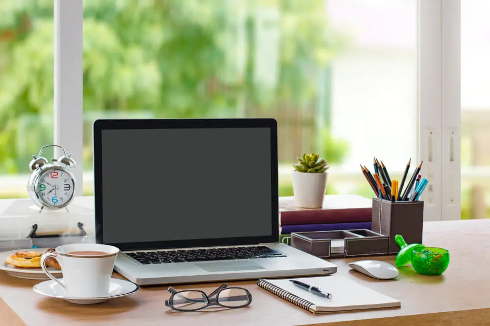 Photo of a typical home office with a laptop, clock, pencils, notepad, and cup of coffee. When asked whether they prefer on-site or remote transcribing work, transcribers said that they like having full control over their workspace while working remotely.