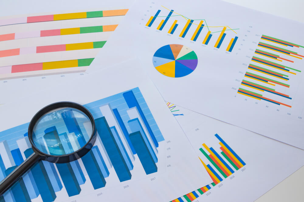 Photo of colorful survey results printed out on paper, and a magnifying glass, like the 2005 Transcriber Insights Survey