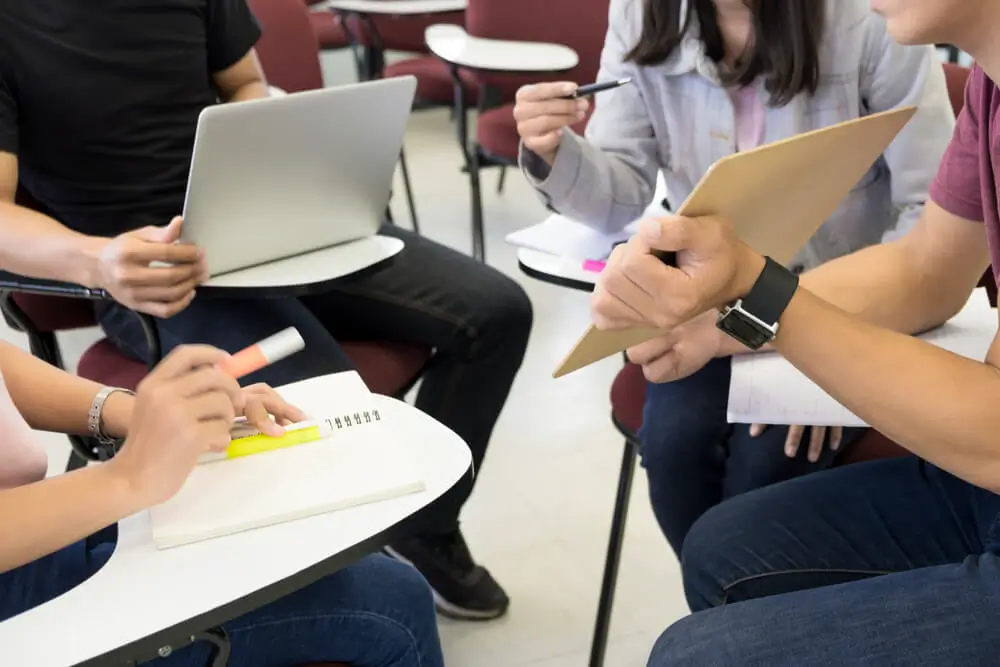 Photo of a group of students collaborating on a project, while a transcriber joins the circle. The stronger atmosphere of collaboration is a major factor in transcriber choice between on-site and remote work.