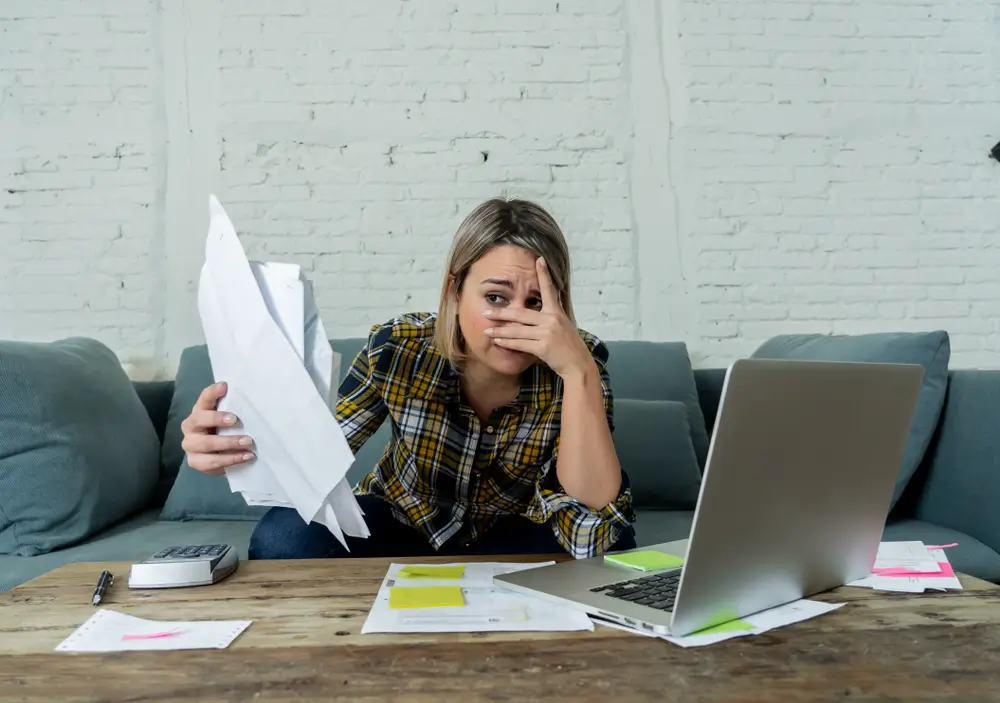 Photo of a young woman holding a stack of papers, partially covering her eyes in fear of her personal finance situation