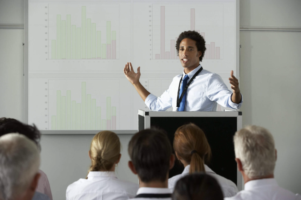 Young businessman delivering presentation at a conference in which real-time transcription services may require prep time