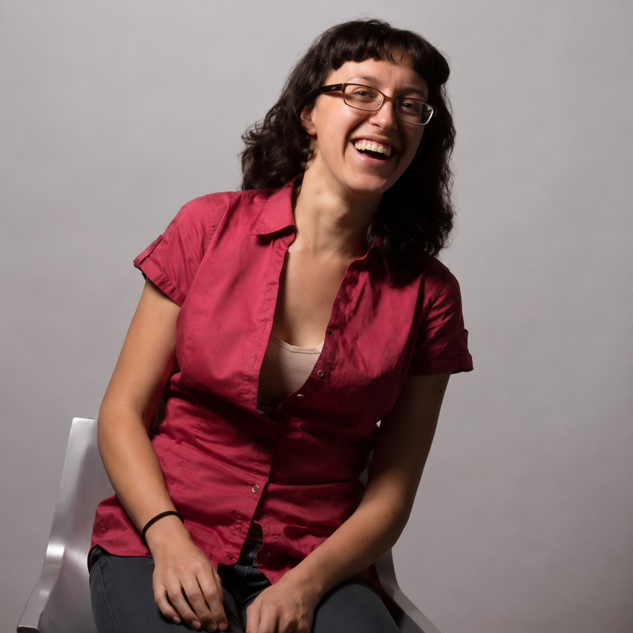 Seated woman with glasses laughing during a studio portrait session.